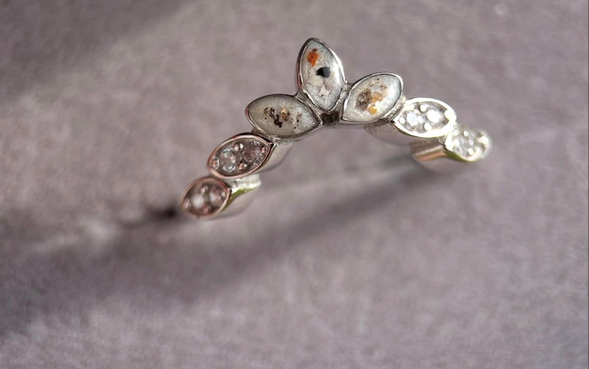 Silver ring with embedded stones on a gray background with ashes 