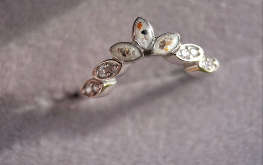 Silver ring with embedded stones on a gray background with ashes 