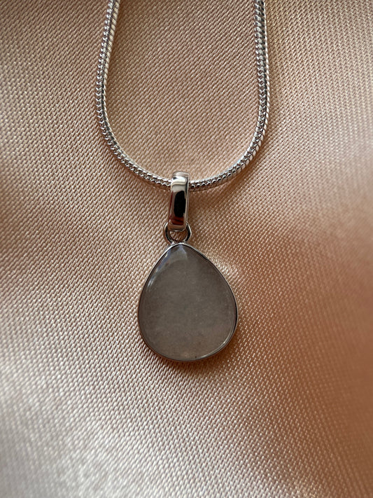 Silver necklace with a heart-shaped pendant on a beige fabric background